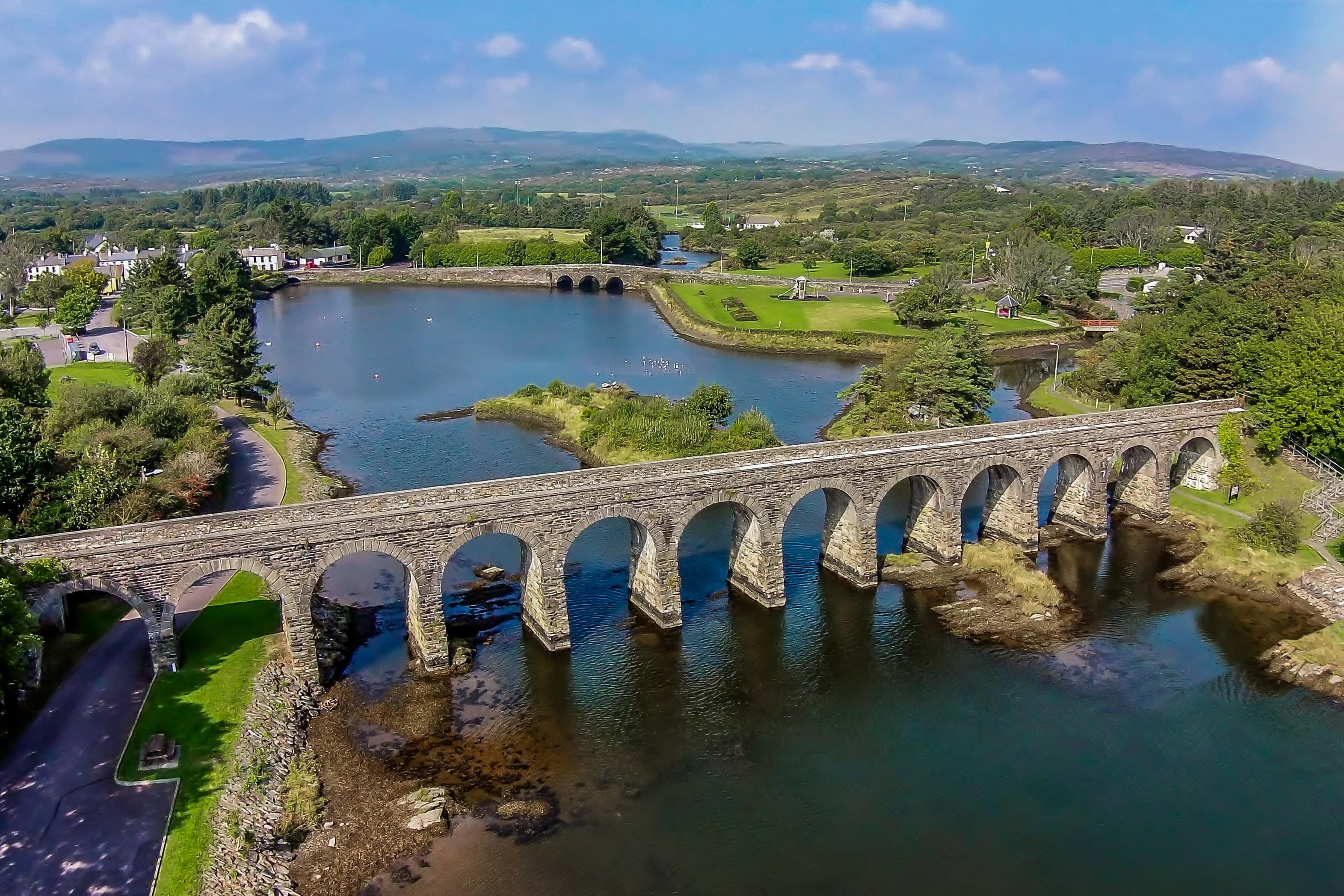 Aerial view across Ballydehob’s stone railway viaduct, harbour and village towards the hills of West Cork
